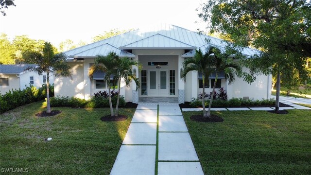 view of front facade with metal roof, french doors, stucco siding, a front lawn, and a standing seam roof