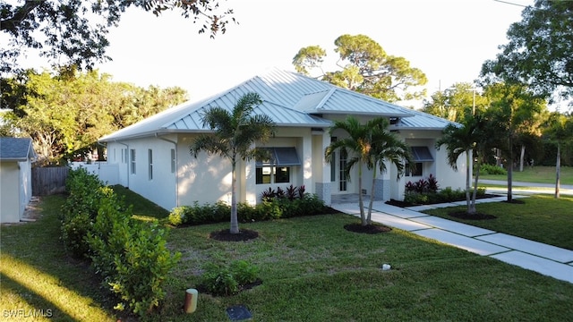 view of front of home featuring stucco siding, a front yard, a standing seam roof, fence, and metal roof