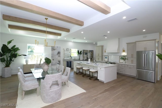 dining space featuring beverage cooler, light wood finished floors, beam ceiling, and recessed lighting