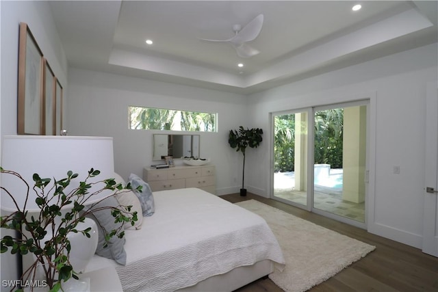 bedroom featuring access to exterior, multiple windows, a tray ceiling, and wood finished floors