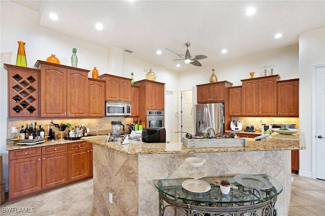 kitchen featuring ceiling fan, a large island with sink, decorative backsplash, a breakfast bar, and appliances with stainless steel finishes