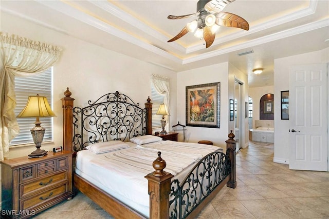 tiled bedroom with ceiling fan, ornamental molding, a tray ceiling, and ensuite bath