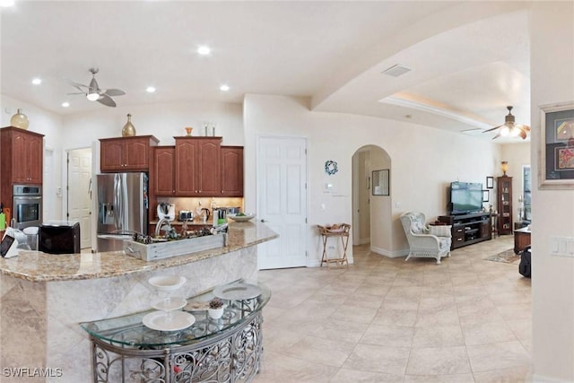 kitchen featuring a kitchen breakfast bar, ceiling fan, light stone counters, and stainless steel fridge with ice dispenser