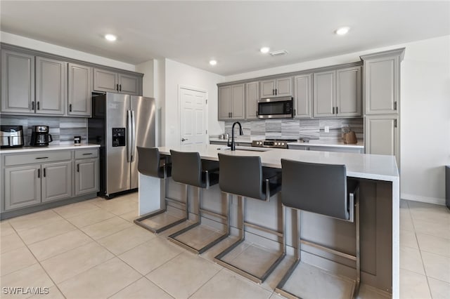 kitchen with decorative backsplash, gray cabinets, stainless steel appliances, and a kitchen island with sink