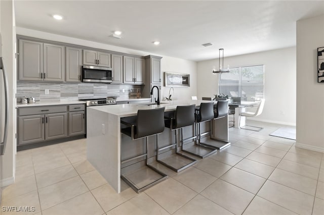 kitchen with tasteful backsplash, gray cabinets, a kitchen island with sink, and light tile patterned floors