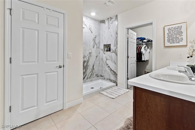 bathroom with tile patterned flooring, a tile shower, and vanity