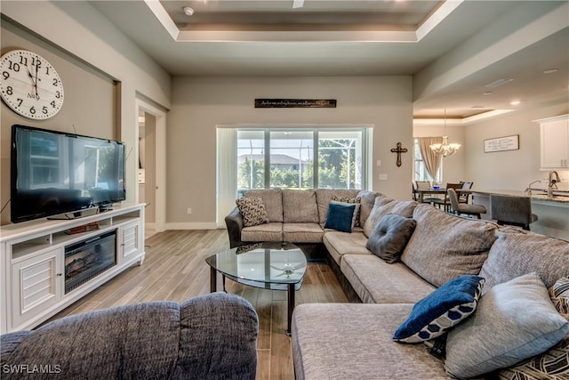 living room with a tray ceiling, light hardwood / wood-style flooring, an inviting chandelier, and sink