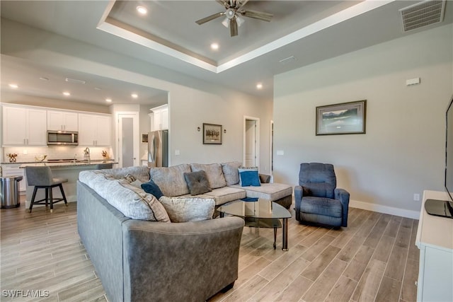 living room with a tray ceiling, light hardwood / wood-style flooring, ceiling fan, and sink