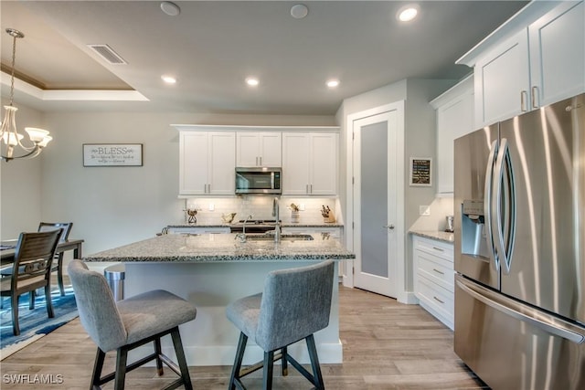 kitchen with white cabinets, appliances with stainless steel finishes, light hardwood / wood-style floors, and light stone counters