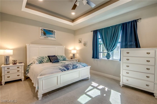 bedroom featuring a raised ceiling, ceiling fan, and light colored carpet