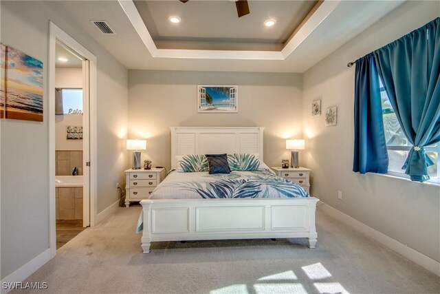 bedroom with ceiling fan, a raised ceiling, light carpet, and ensuite bath