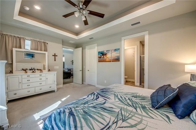 carpeted bedroom featuring a raised ceiling, ceiling fan, and ensuite bathroom