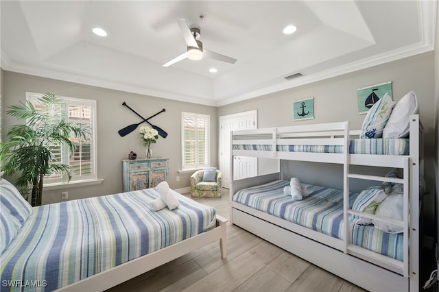 bedroom with hardwood / wood-style flooring, a raised ceiling, ceiling fan, and crown molding