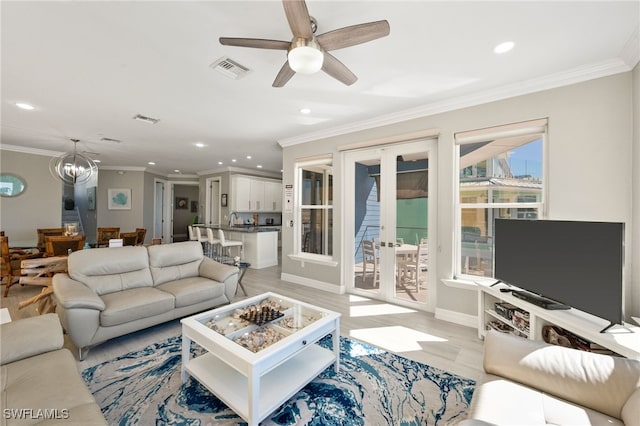 living room featuring ceiling fan with notable chandelier, light wood-type flooring, ornamental molding, and french doors