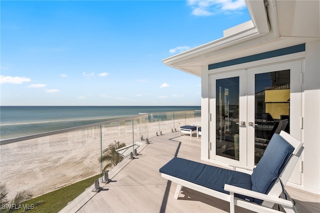 view of patio / terrace with a beach view, french doors, a water view, and a balcony