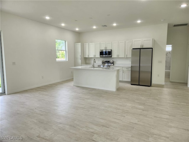 kitchen featuring white cabinetry, sink, light hardwood / wood-style flooring, a kitchen island with sink, and appliances with stainless steel finishes