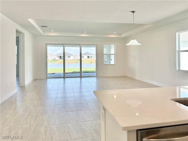 kitchen with light stone countertops, light tile patterned flooring, decorative light fixtures, stainless steel dishwasher, and a raised ceiling