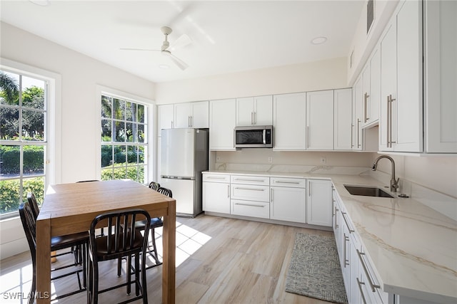 kitchen featuring white cabinetry, light stone countertops, sink, light hardwood / wood-style flooring, and refrigerator