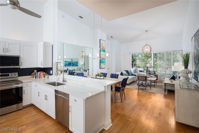 kitchen featuring kitchen peninsula, appliances with stainless steel finishes, high vaulted ceiling, and sink