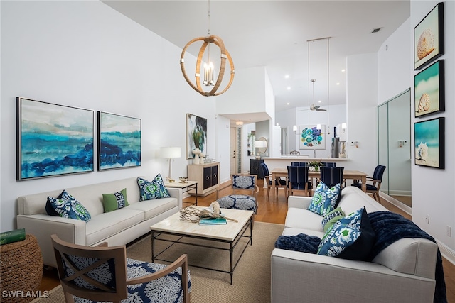 living room with high vaulted ceiling, wood-type flooring, and ceiling fan with notable chandelier