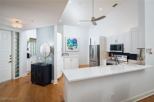 kitchen with kitchen peninsula, ceiling fan, light wood-type flooring, appliances with stainless steel finishes, and white cabinetry