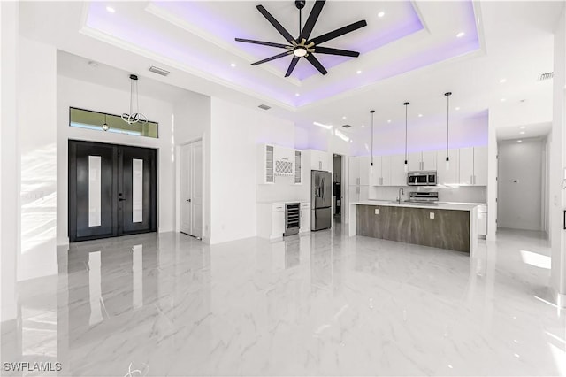 unfurnished living room with a raised ceiling, ceiling fan, sink, elevator, and wine cooler