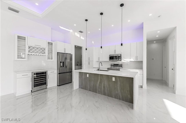 kitchen featuring beverage cooler, decorative light fixtures, a kitchen island with sink, white cabinets, and appliances with stainless steel finishes