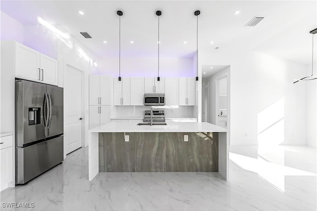 kitchen featuring appliances with stainless steel finishes, white cabinetry, hanging light fixtures, and an island with sink