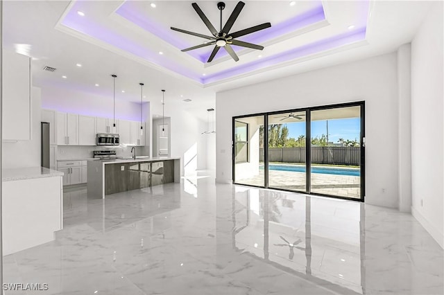 unfurnished living room with a tray ceiling, ceiling fan, and sink