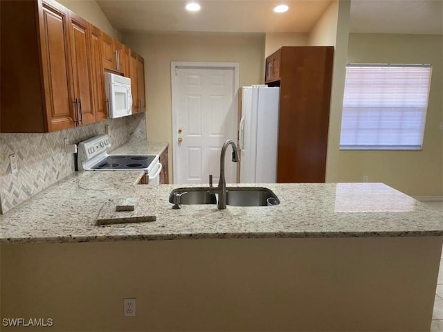 kitchen featuring kitchen peninsula, light stone countertops, sink, and white appliances