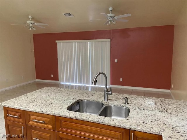 kitchen with light stone counters, sink, ceiling fan, and light tile patterned floors