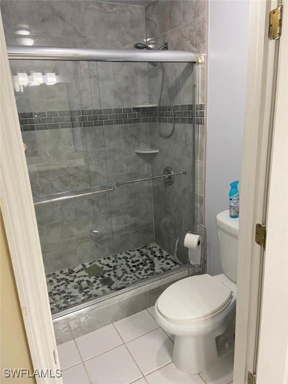 bathroom with tile patterned flooring, toilet, and a shower with shower door