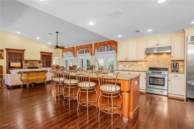 kitchen with lofted ceiling, dark wood-type flooring, light stone countertops, an island with sink, and stainless steel appliances