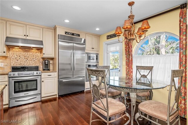 kitchen with light stone countertops, dark hardwood / wood-style flooring, cream cabinets, built in appliances, and hanging light fixtures