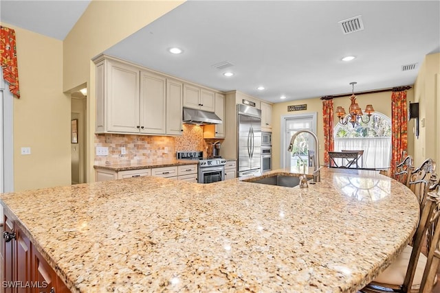 kitchen with cream cabinets, light stone counters, sink, and appliances with stainless steel finishes