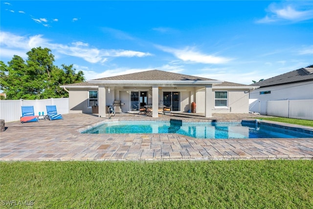 rear view of property featuring a lawn, a patio area, and a fenced in pool