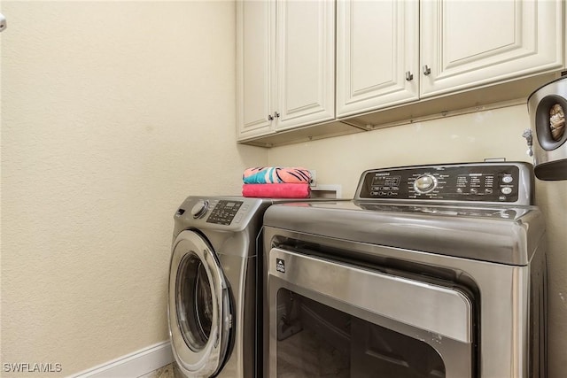 clothes washing area with washer and dryer and cabinets