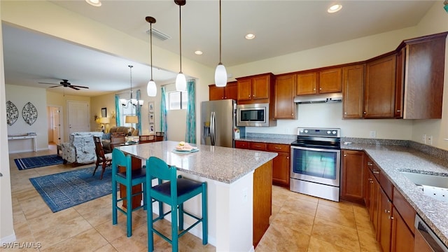 kitchen with a kitchen breakfast bar, decorative light fixtures, a kitchen island, ceiling fan with notable chandelier, and appliances with stainless steel finishes