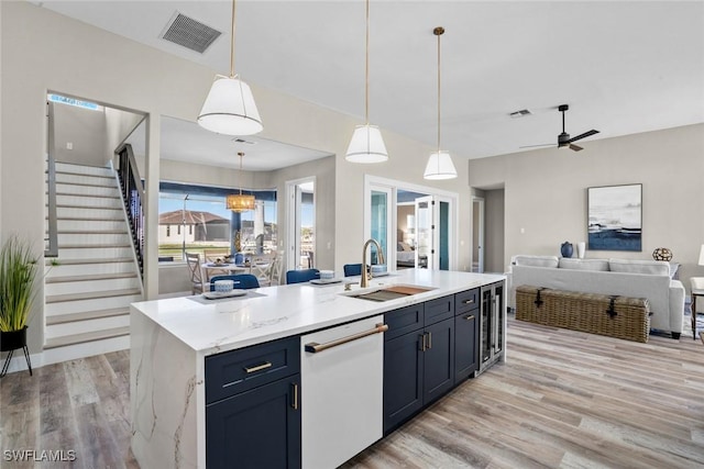 kitchen with ceiling fan with notable chandelier, white dishwasher, decorative light fixtures, light hardwood / wood-style flooring, and a center island with sink