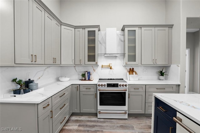 kitchen featuring light stone countertops, wall chimney range hood, range, tasteful backsplash, and light wood-type flooring