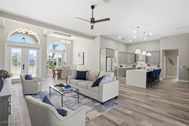 living room featuring sink, french doors, a towering ceiling, ceiling fan with notable chandelier, and light wood-type flooring