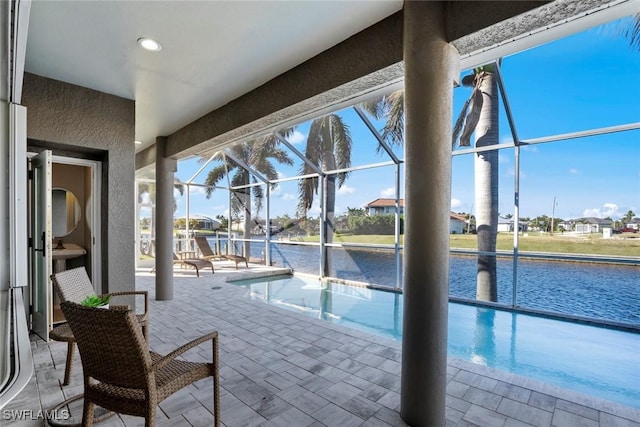 view of pool featuring glass enclosure, a patio area, and a water view