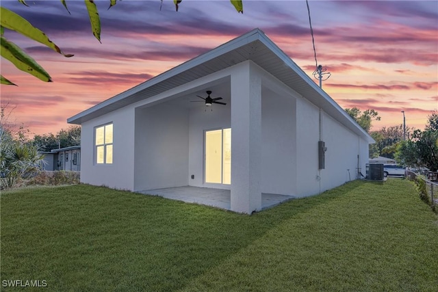 property exterior at dusk featuring ceiling fan, a yard, a patio, and central AC