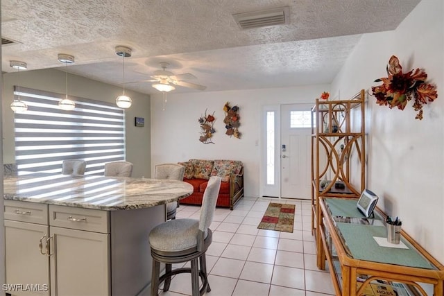 kitchen with a kitchen breakfast bar, light stone counters, decorative light fixtures, a textured ceiling, and light tile patterned floors