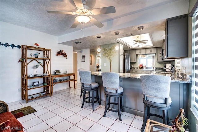 kitchen with a textured ceiling, gray cabinets, light stone countertops, and stainless steel appliances