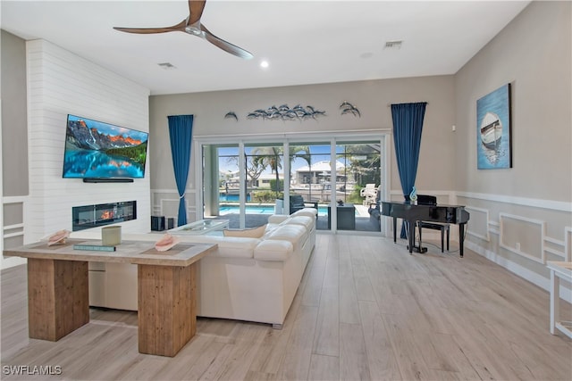 living room featuring a large fireplace, light hardwood / wood-style flooring, and ceiling fan