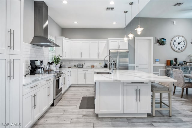 kitchen with sink, stainless steel appliances, white cabinetry, and wall chimney range hood