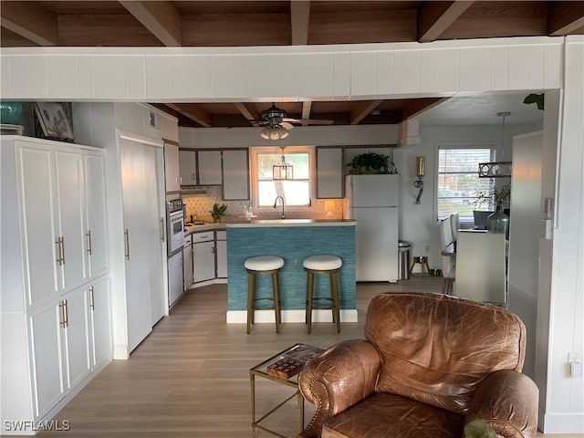 kitchen featuring refrigerator, beam ceiling, wall oven, tasteful backsplash, and light wood-type flooring