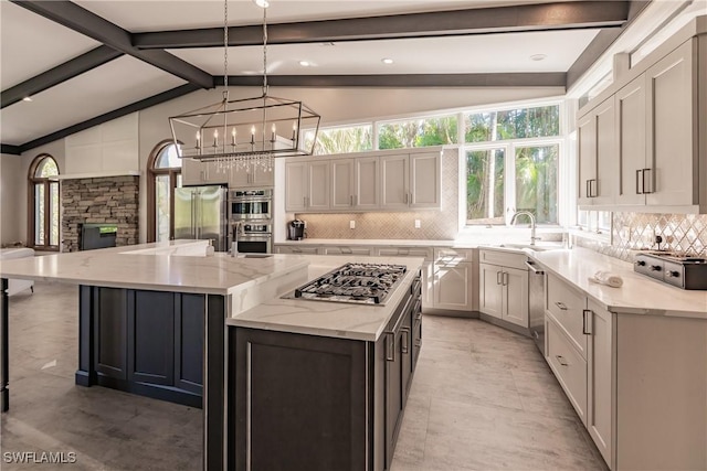 kitchen featuring a large island with sink, pendant lighting, stainless steel appliances, light stone countertops, and decorative backsplash