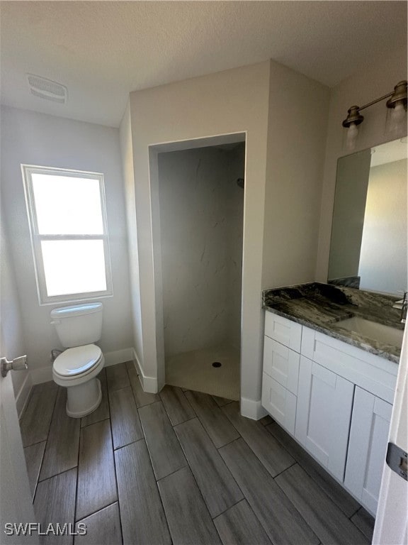 bathroom with a shower, vanity, a textured ceiling, and toilet